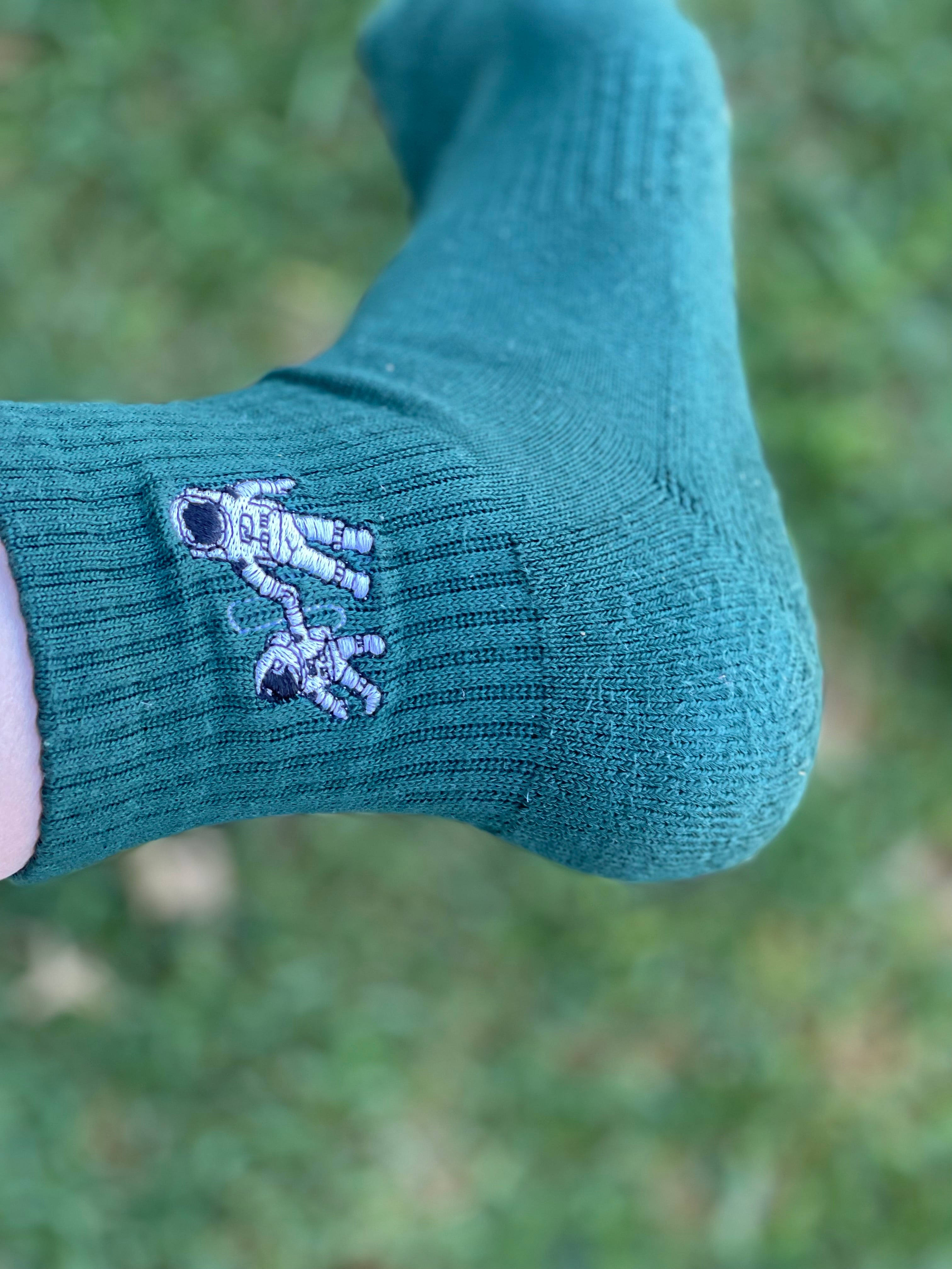 Small Steps Co. deep green bamboo sock with embroidered astronaut duo, held outdoors