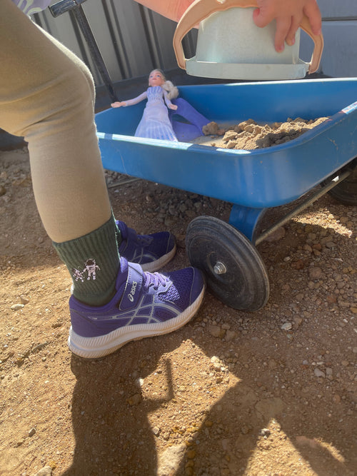 Kid wearing Small Steps Co. green astronaut socks with sneakers while playing outside