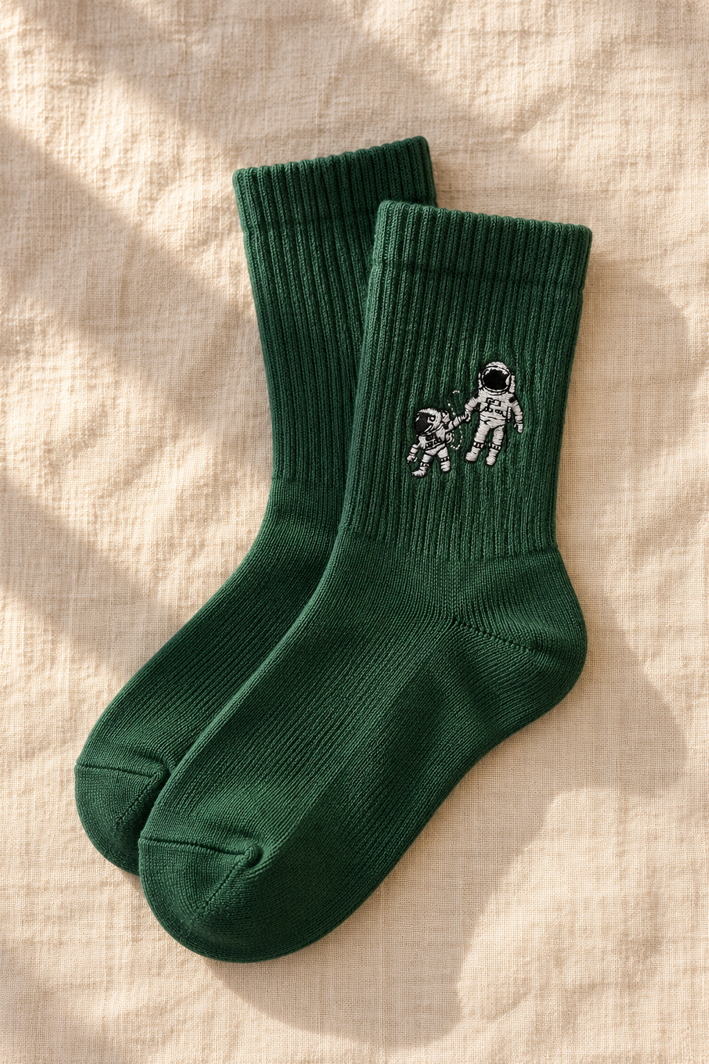 Small Steps Co. big kids deep green bamboo crew socks with astronaut emblem, on linen