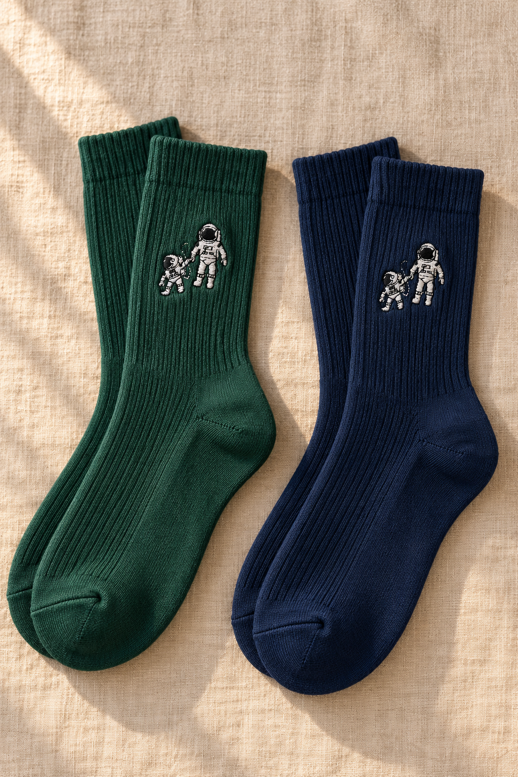 Small Steps Co. men's bamboo crew socks in deep green and navy with embroidered astronaut emblem, on linen