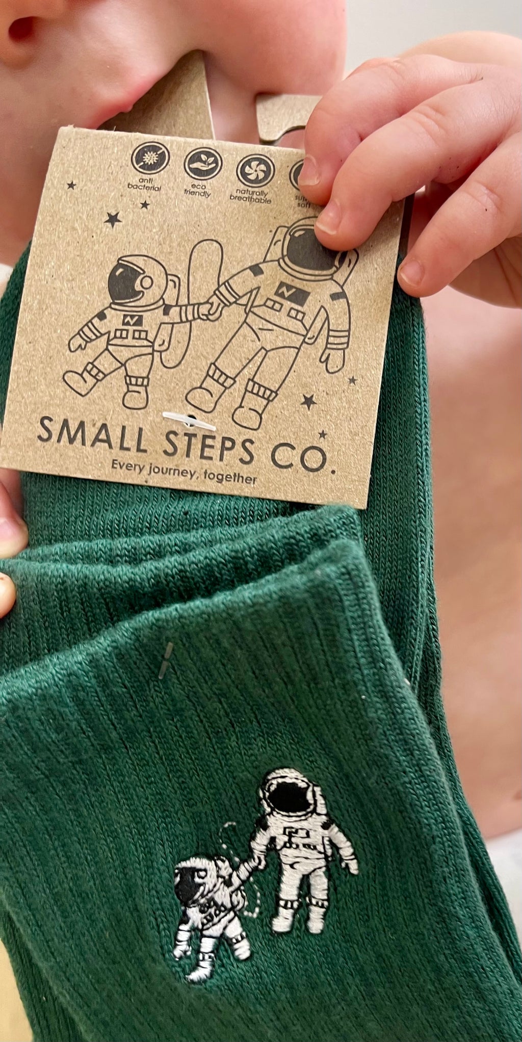 Child holding Small Steps Co. deep green bamboo socks with kraft tag